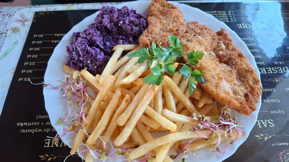 Talerz ze schabowym, frytkami i czerwoną kapustą, postawiony na drukowanym menu bistro